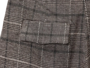 Détail de la texture en laine mélangée à carreaux marron et de la poche à rabat du pantalon