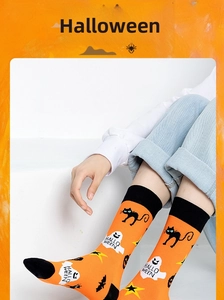 Detail of Halloween crew socks featuring black cats, ghosts, and bats on orange knit fabric