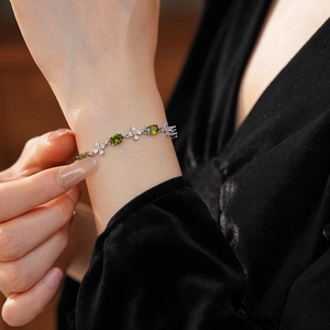 Close-up of olive green oval gemstone bracelet with white floral accents on model wrist