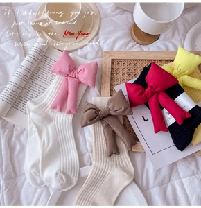 Flat lay of cotton slouch socks with large 3D bows in white, beige, black, and yellow