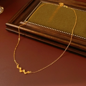 Macro detail of a vintage gold-brushed necklace with textured wave pendant on red leather