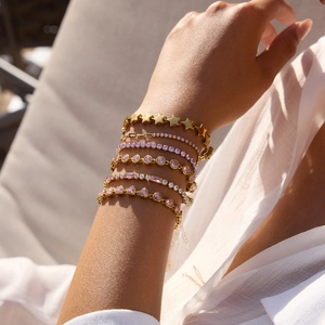 Close-up of stacked gold-plated bracelets with pink zircon hearts and stars on wrist