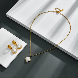 Close-up of gold clover necklace and earrings with pearl shell inlay on white stones