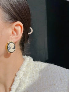 Detail view of vintage gold-framed cameo earrings with white silhouette on model