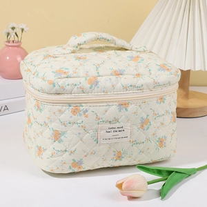 Quilted floral makeup bag with top handle and soft beige fabric in a home setting