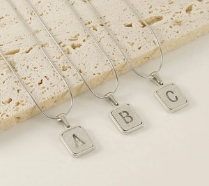 Macro detail of three silver snakeskin chains with frosted A, B, and C letter pendants