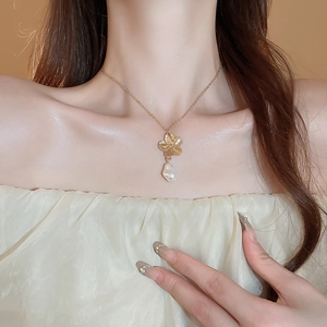 Detail of vintage gold flower necklace with white baroque pearl drop worn on neck