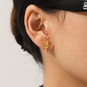 Close-up of 18k gold leaf-shaped earrings worn by a model in soft lighting