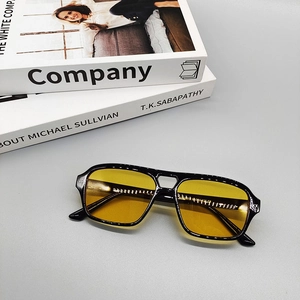 Gafas de sol de aviador retro con montura negra y lentes amarillas sobre libros de moda