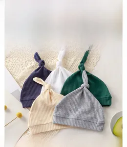Close-up of five colorful ribbed knit baby hats with top knots on a decorative lace background