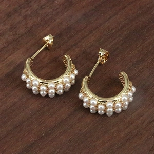Detailed macro view of C-shaped gold earrings featuring double row white pearl inlay