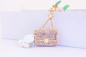 Detail of gold bag keychain featuring sparkling rhinestones, white pearl, and rose charm