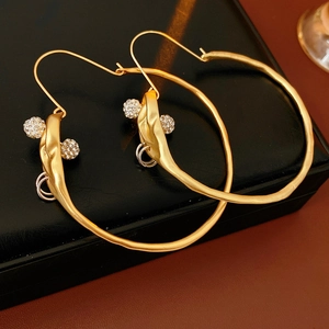 Detail of gold matte hoop earrings with rhinestone-encrusted spheres on a black case