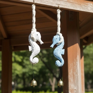 Blue and white seahorse wind chimes with gold bells hanging on a wooden beam outdoors