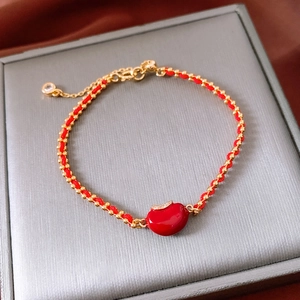 Detail eines roten geflochtenen Armbands mit 18 Karat vergoldeten Perlen und Apfelanhänger
