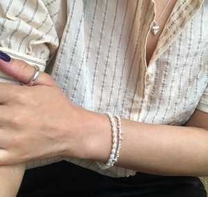 Close-up of layered 925 silver pearl bracelet with heart pendant and ring on model