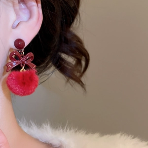 Dettaglio dell'orecchino con fiocco rosso e pompon indossato da una modella in inverno