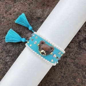 Close-up of a handmade cyan woven bracelet featuring a crystal bear and blue tassels