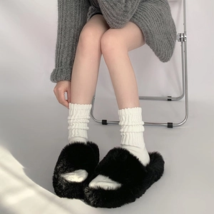 Women cozy white knitted slouch socks paired with black fuzzy plush home slippers