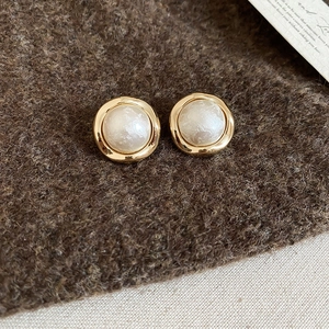 Detailed close-up of gold-plated geometric pearl stud earrings on soft cashmere fabric