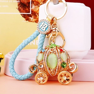 Detail view of golden pumpkin carriage keychain with green crystals and blue woven cord