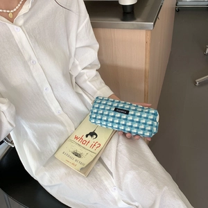 Détail d'une trousse en tweed bleu et blanc tenue par un modèle dans un style épuré