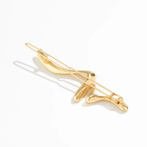Detail of a minimalist gold liquid metal hair clip featuring a fluid wavy surface design
