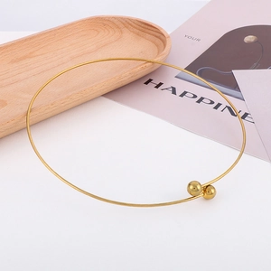 Minimalist golden stainless steel choker necklace with polished balls on a wooden tray
