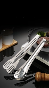 Close-up of polished stainless steel kitchen tongs with oil drainage holes and ergonomic grip