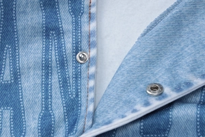 Detailed macro view of denim print fabric featuring two silver metal snap buttons and stitching