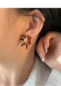 Close-up of elegant red enamel flower earring with gold edges and zircon on woman's ear