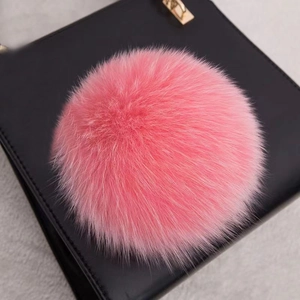 Gros plan d'un pompon en fourrure véritable rose sur un sac à main en cuir noir