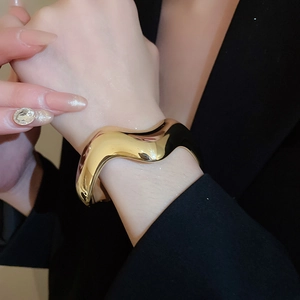 Primo piano di un ampio bracciale a polsino dorato ondulato indossato sopra un abito scuro