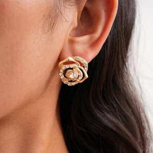 Detail of rose flower gold earrings with sparkling crystals worn on a model ear