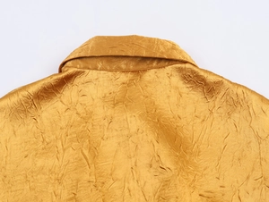 Detail van gouden satijnen jurk met kreukeltextuur en elegante stiksels aan de reverskraag