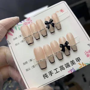 Faux ongles faits main rose nude avec pointes françaises noires et nœuds en cristal