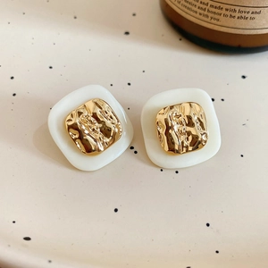 Detailed close-up of retro square earrings with textured gold inlay on cream base