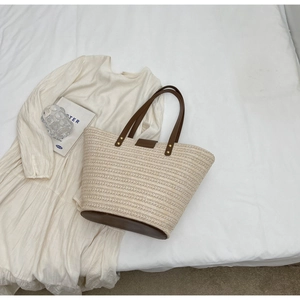 Close-up of beige woven straw tote with brown PU leather straps and metal buckle closure