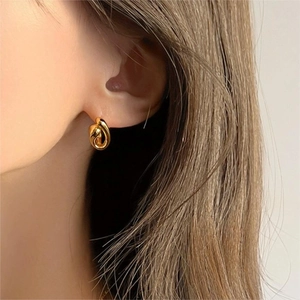 Minimalist twisted gold hoop earring worn by a model in a close-up side profile view