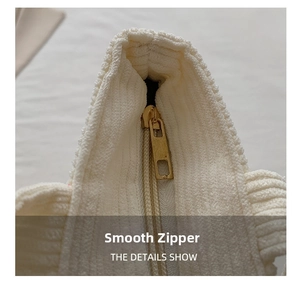 Detailed close-up of smooth gold zipper and white corduroy texture on minimalist tote bag