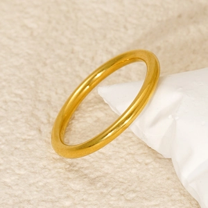 Minimalist gold stainless steel band ring displayed on white stone against beige background