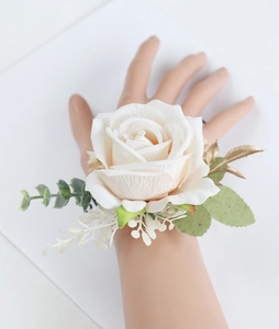 Detailed view of a white artificial rose wrist corsage with golden leaves and greenery
