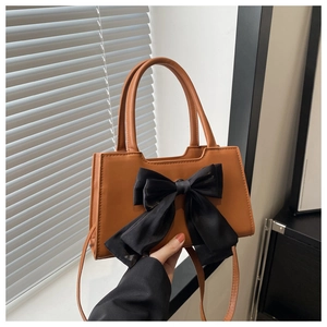 Detail of a brown PU handbag featuring a large black satin bow and a top handle