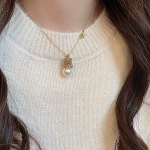 Close-up of a necklace with a brown flocked bear pendant and pearl on a golden chain