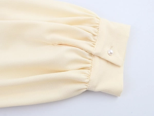 Detail of beige lantern sleeve cuff with pleats and elegant pearl button closure