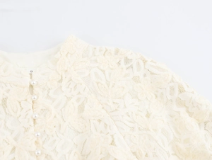 Détail de la robe en dentelle beige avec broderie florale, bouton perle et étiquette