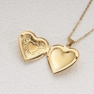 Polished gold heart locket necklace with vintage engraved patterns on a white background