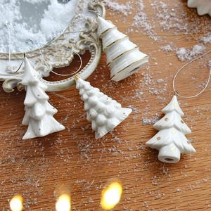 White ceramic Christmas tree ornaments with gold accents on rustic wood background