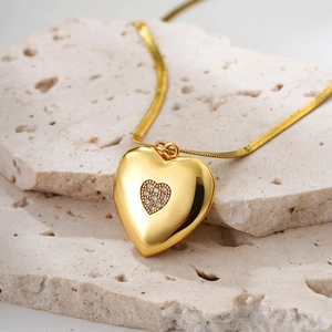 Detail view of 18K gold plated heart locket pendant with diamonds on beige stone