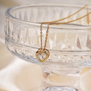 Elegant gold heart pendant necklace with clear zircon displayed on glass vessel
